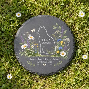 May include: A round, dark gray slate memorial stone featuring a white etched silhouette of a cat surrounded by colorful wildflowers and a butterfly. The text reads LUNA 2020-2026, Forever Loved, Forever Missed My Sweet Girl, and a small paw print heart.