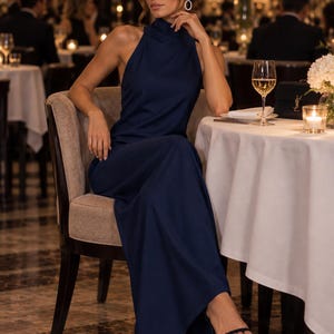 Könnte beinhalten: Ein bodenlanges, ärmelloses Kleid in Marineblau mit hohem Stehkragen und einem körperbetonten Oberteil, das in einen langen, geraden Rock übergeht. Das Kleid besteht aus einem glatten, einfarbigen Stoff und wird mit schwarzen Riemchensandalen kombiniert.