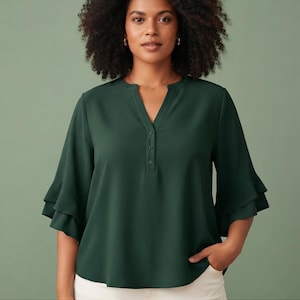 Puede incluir: Una blusa de color verde oscuro con escote en V, tres botones pequeños, mangas hasta el codo con dos niveles de volantes y un dobladillo ligeramente curvado. El texto GATHERED BLOUSE aparece en la parte inferior de la imagen.