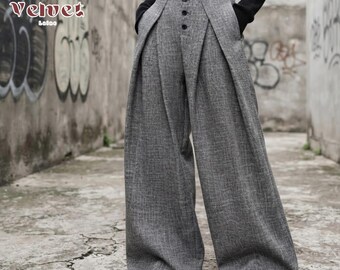 May include: High-waisted wide-leg trousers in a textured gray fabric. The pants feature a front button closure with four visible dark buttons and deep pleats extending from the waistband. The garment is paired with a black long-sleeved top.