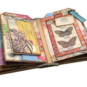 Op de afbeelding: Een open journal met pagina's versierd met vintage botanische illustraties, waaronder een close-up van een paarse bloem, en een pagina met een ingelijste illustratie van drie vlinders met de labels "Type A", "Type B" en "Type C".