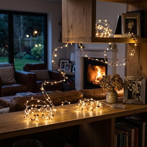 May include: A string of warm white LED fairy lights featuring small metallic star-shaped accents. The thin, flexible copper-colored wire is coiled on a wooden surface and draped across a shelf, creating a glowing decorative lighting display.