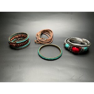 May include: A collection of four bracelets: one multi-strand wrap bracelet with brown beads and turquoise accents, a tan leather wrap bracelet, a thin bangle with turquoise beads, and a silver-toned coil bracelet with red and turquoise beads.
