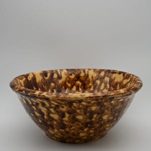 Może przedstawiać: Okrągła ceramiczna miska do mieszania z nakrapianym wzorem malowanym gąbką, składającym się z ciemnobrązowych i beżowych plam na całej powierzchni wewnętrznej i zewnętrznej. Miska posiada szeroki, gruby, zaokrąglony brzeg oraz głęboką, pochyłą czaszę.