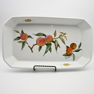 May include: A rectangular white ceramic serving tray with beveled edges. The center features a painted illustration of a branch with several peaches and green leaves. Two small green olives are painted near the top and bottom edges.