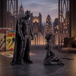 May include: A black Batman figurine standing upright in a tactical suit with a cape, positioned next to a black Catwoman figurine kneeling on the ground. Both figures are rendered in a matte black finish, capturing their iconic comic book character designs.