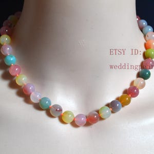 May include: A multi-coloured gemstone necklace with round beads in shades of pink, yellow, green, and orange. The necklace is strung on a thin orange cord.
