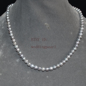 May include: A single strand necklace composed of small, round, light grey pearls with a subtle iridescent sheen. The text "ETSY ID: weddingpearl" is printed in the centre of the display. The pearls are uniform in size and arranged in a circular shape.