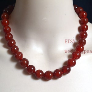 May include: A red carnelian gemstone necklace with round beads. The necklace is on a white mannequin.