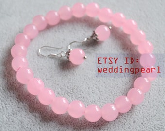 Puede incluir: Un brazalete y pendientes a juego de piedras preciosas rosas. El brazalete está hecho de cuentas redondas y los pendientes son de estilo colgante con una sola cuenta redonda.