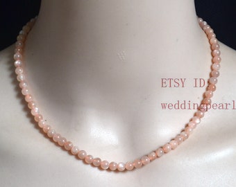 Könnte beinhalten: Eine zarte Halskette aus kleinen, runden, pfirsichfarbenen Perlen. Die Halskette befindet sich auf dem Hals einer Puppe. Der Text "ETSY ID weddingpearl" ist auf dem Bild sichtbar.