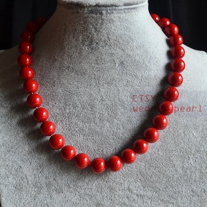 May include: A red beaded necklace made of large, round beads. The necklace is displayed on a gray mannequin.