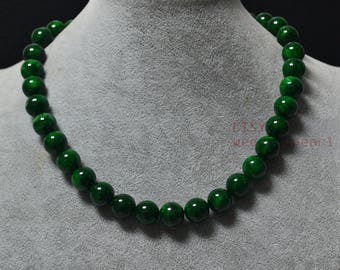 May include: A necklace of large, round, polished green beads. The beads are strung together to form a necklace. The necklace is displayed on a gray mannequin. The beads have a glossy finish.