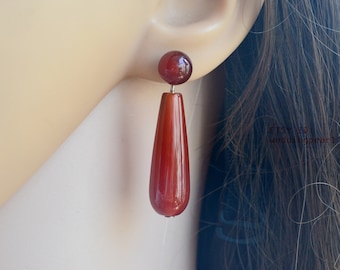 May include: A pair of dangle earrings with a teardrop-shaped carnelian stone and a round carnelian stone at the top. The earrings are made of silver.