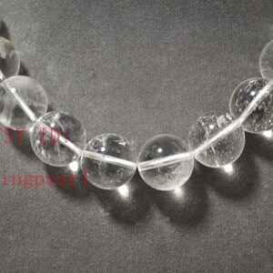 May include: A strand of clear quartz beads, each bead is round and smooth. The beads are strung on a white thread.
