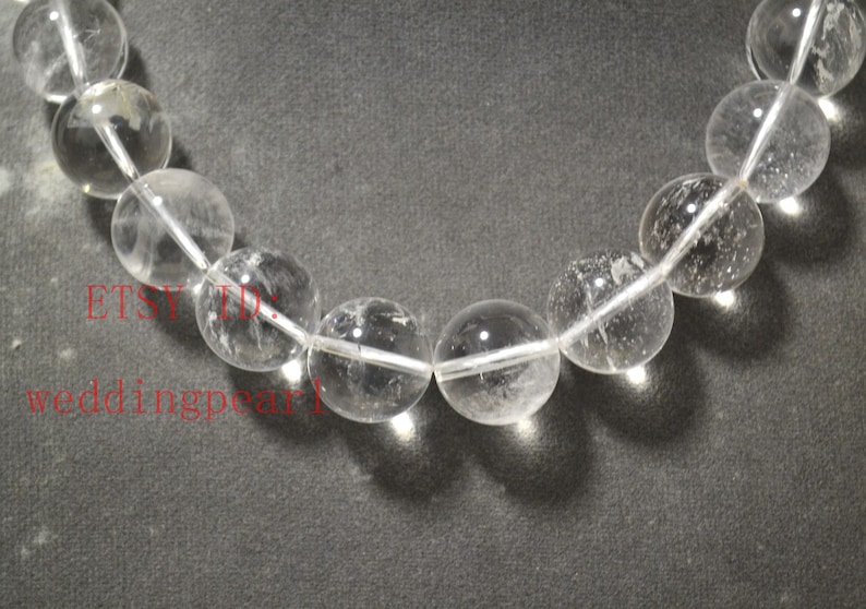 May include: A strand of clear quartz beads, each bead is round and smooth. The beads are strung on a white thread.