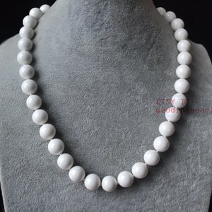 Puede incluir: Un collar de perlas blancas con cuentas grandes y redondas. El collar se muestra en un busto de maniquí gris.