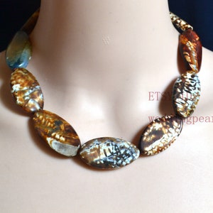 May include: A necklace made of oval-shaped agate beads with brown, white, and blue patterns. The beads are strung on a clear cord.