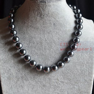 Puede incluir: Un collar de cuentas gris oscuro con cuentas grandes y redondas. El collar se exhibe en un maniquí gris. El nombre de la tienda Etsy "weddingpearl1" es visible en la imagen.