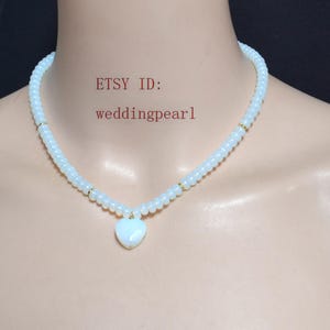 Puede incluir: Un delicado collar de cuentas blancas con un colgante en forma de corazón. El collar presenta pequeñas cuentas redondas y detalles dorados. El ID de Etsy es weddingpearl.