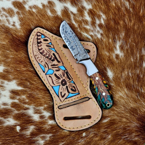 Hand-forged Damascus steel blade paired with turquoise-inlaid tooled leather sheath — a working knife that doubles as wearable Western art.