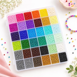 Peut inclure: Une boîte de rangement rectangulaire en plastique transparent divisée en trente-cinq compartiments carrés, chacun rempli de petites perles rondes en verre dans une variété de couleurs unies, notamment rose, rouge, orange, jaune, bleu, vert, marron et noir.