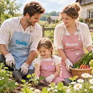 May include: Three matching aprons with vertical stripes. One blue apron features the embroidered text Daddy, while two red aprons feature the embroidered text Mama and Luna. Each apron includes a front pocket, adjustable neck straps, and a small label.