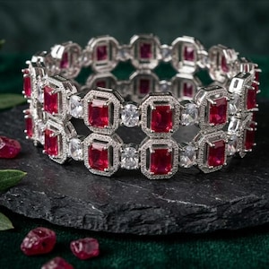 Puede incluir: Una pulsera de tono plateado con dos filas paralelas de piedras rectangulares de color rojo intenso que alternan con piedras redondas transparentes. Cada piedra roja está engastada en un marco octogonal plateado texturizado.