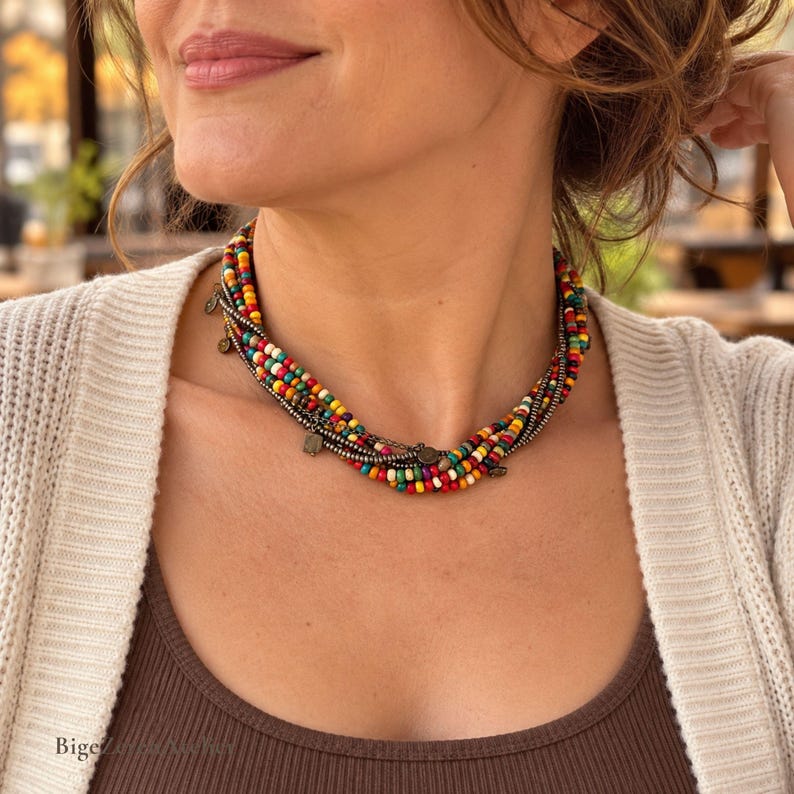 May include: A multi-strand choker necklace featuring small, vibrant beads in red, yellow, green, and blue, interspersed with metallic silver-toned spacer beads and small, dangling circular metal charms along the length of the strands.