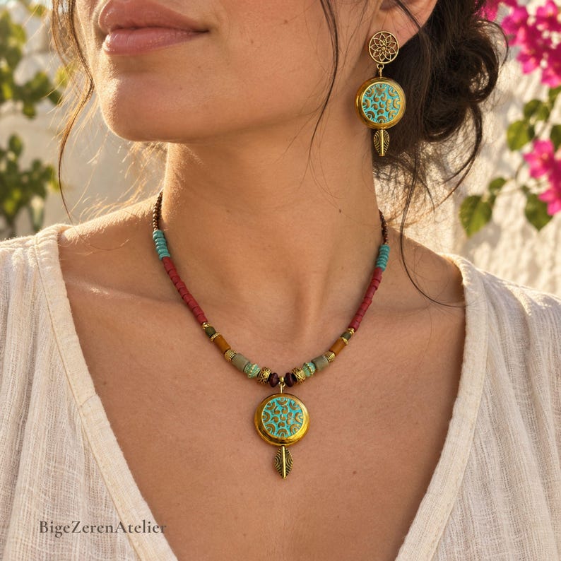 May include: A gold-toned necklace and matching earring set featuring circular pendants with turquoise and gold filigree patterns. The necklace includes red, turquoise, and brown beads, while the earring has a floral-shaped stud.