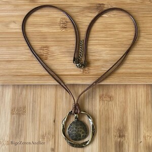 Full view of a brown double cord necklace with antique bronze tone round pendant, adjustable chain and lobster clasp on a wooden background.