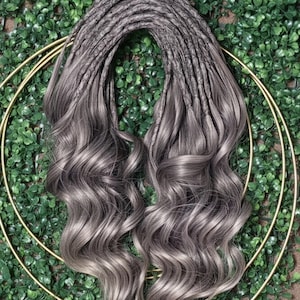 May include: A set of synthetic hair extensions featuring a dark gray to light ash gray ombre color transition. The top section consists of textured, braided-style roots that flow into long, loose, voluminous waves with a smooth, shiny finish.