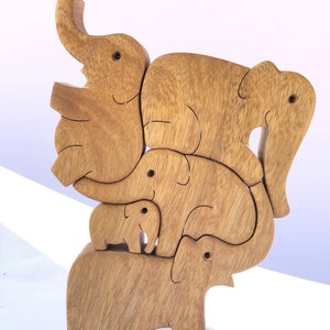 A handcrafted wooden puzzle featuring a family of five elephants, nestled together in a compact, upright tower. The interlocking pieces show various sizes of elephants, with a smooth finish, positioned on a light background.