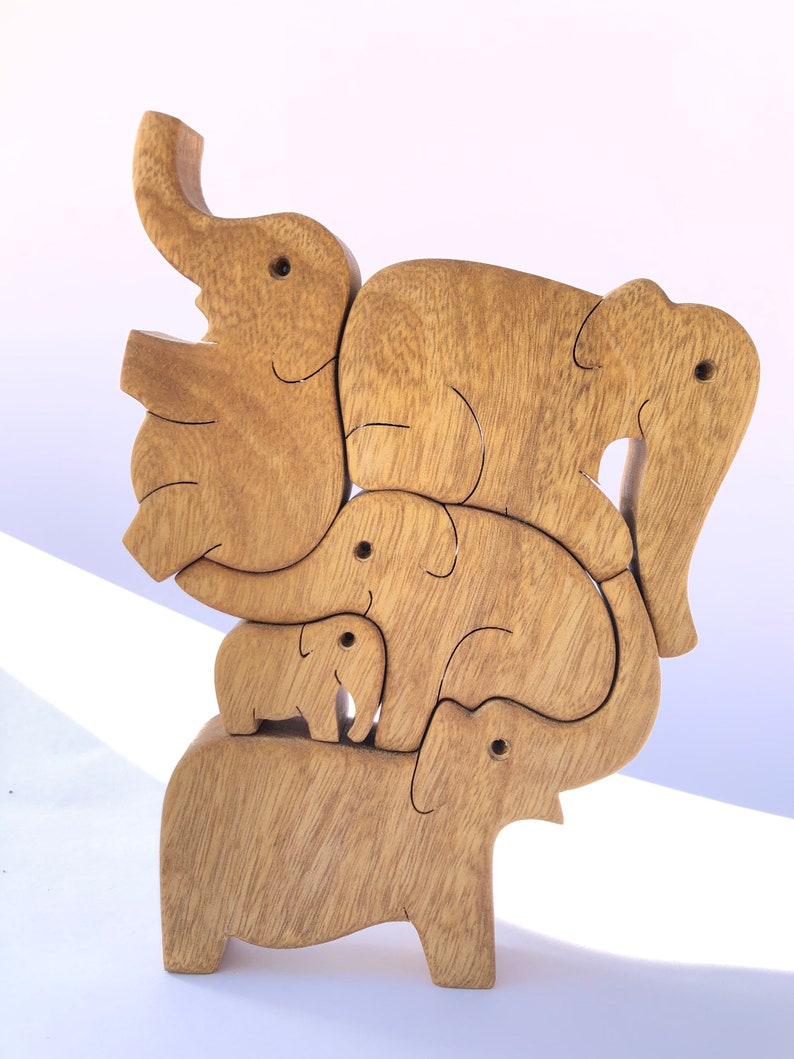 A handcrafted wooden puzzle featuring a family of five elephants, nestled together in a compact, upright tower. The interlocking pieces show various sizes of elephants, with a smooth finish, positioned on a light background.