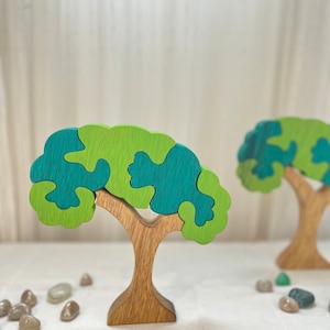 May include: A wooden puzzle tree toy with a brown trunk and green and blue leaves. The leaves are shaped like puzzle pieces and can be removed and rearranged.