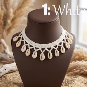May include: A white crocheted choker necklace featuring a series of dangling natural tan cowrie shells attached to a woven band. The text 1: White is displayed in the upper right corner of the image, indicating the color of the jewelry piece.