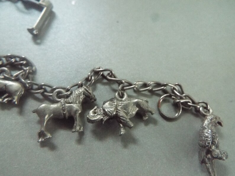 May include: A silver charm bracelet with animal charms, including a horse, elephant, and bird. The bracelet is made of a silver chain with a lobster clasp.