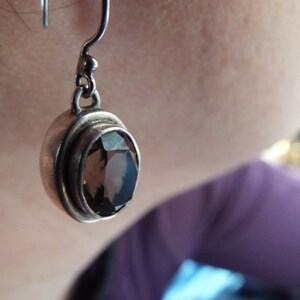 May include: Silver dangle earrings with a round, faceted, smoky quartz gemstone.