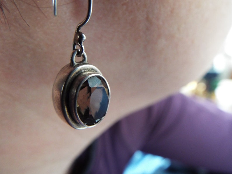 May include: Silver dangle earrings with a round, faceted, smoky quartz gemstone.