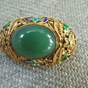 May include: A green jade stone set in a silver filigree ring with blue, green, and white enamel accents.