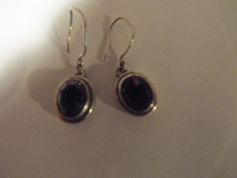 May include: A pair of silver earrings with oval-shaped black gemstones.
