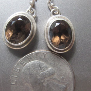 May include: A pair of silver earrings with oval-shaped smoky quartz gemstones.