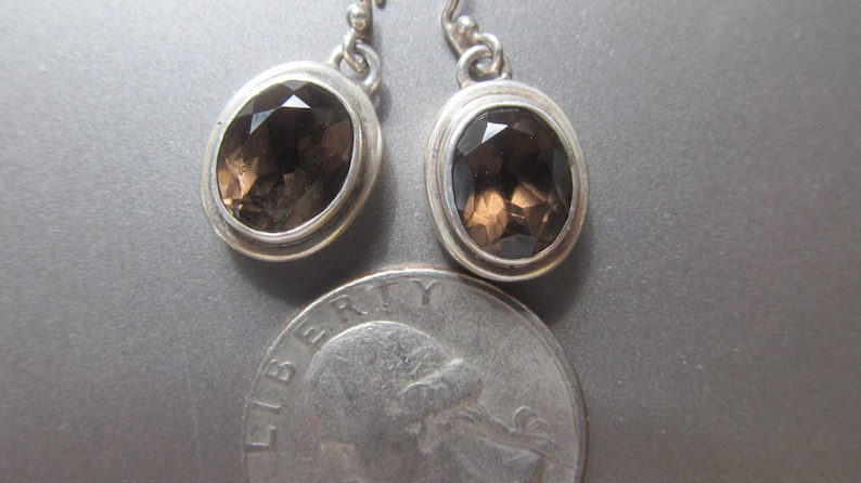 May include: A pair of silver earrings with oval-shaped smoky quartz gemstones.