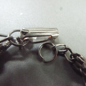 May include: A silver chain bracelet with a lobster clasp closure. The chain is made of small, linked circles. The bracelet features a decorative charm at the end.