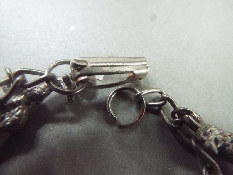 May include: A silver chain bracelet with a lobster clasp closure. The chain is made of small, linked circles. The bracelet features a decorative charm at the end.
