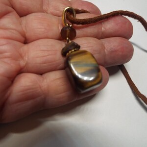 May include: A brown leather cord necklace with a gold pendant featuring a tiger's eye stone.