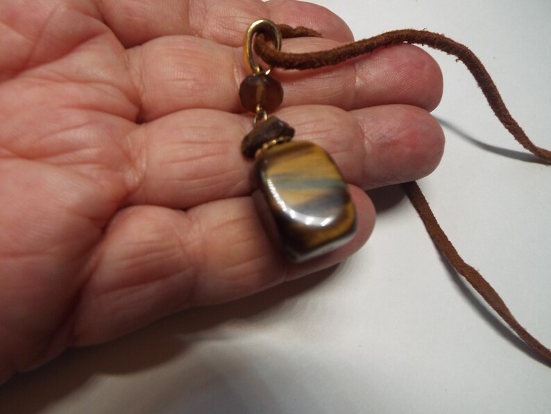 May include: A brown leather cord necklace with a gold pendant featuring a tiger's eye stone.
