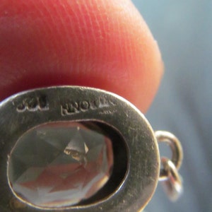 May include: Close-up of a silver pendant with a clear gemstone. The pendant has the inscription "925" and "NORWAY" on the back.