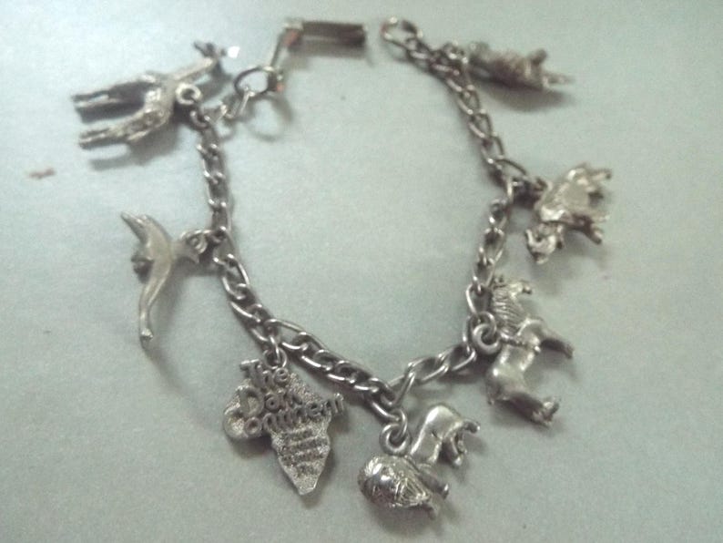 May include: A silver charm bracelet with various animal charms, including a giraffe, a dolphin, a lion, and a hippopotamus. The bracelet also features a charm with the text "The Dark Continent".