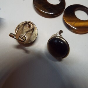 May include: A pair of clip-on earrings with tiger's eye stones. One earring has a round, dark brown stone, while the other has a round, gold-toned setting with a tiger's eye stone.